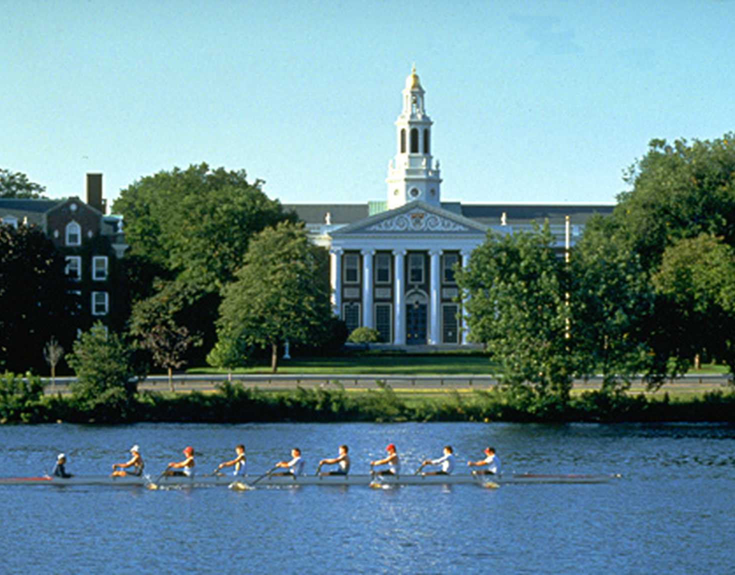 People rowing in a river with a background of Harvard Business School Building